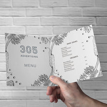 Load image into Gallery viewer, Printed Menu on paper, half folded, held open by customer&#39;s hand. 